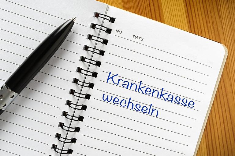 Liniertes Spiralnotizbuch mit schwarzem Kugelschreiber; handschriftlicher Hinweis »Krankenkasse wechseln« in Blau.
