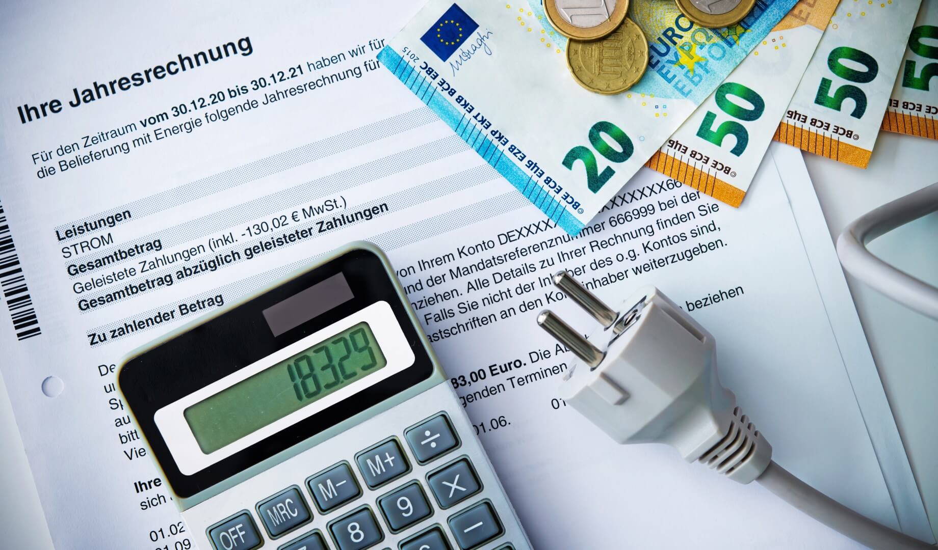 Stromjahresrechnung mit Euro-Geldscheinen, Münzen, Taschenrechner und Stecker: Symbolisiert Energiekosten und Zahlungen.
